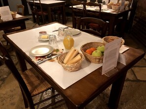 Mesa de comedor dispuesta con pan, fruta, salsas y una carta.