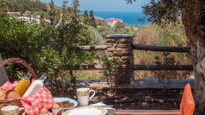 A breakfast setup with a table, plates, cups, and a basket of bread and fruit. - Mainades Maisonettes and Studios (Andros)