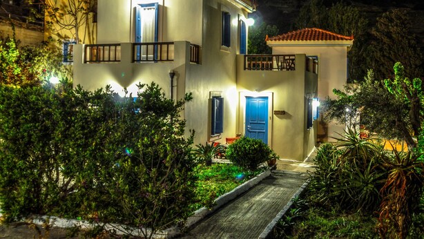 A two-story house with a balcony, a door, and a small garden area. - Mainades Maisonettes and Studios (Andros)