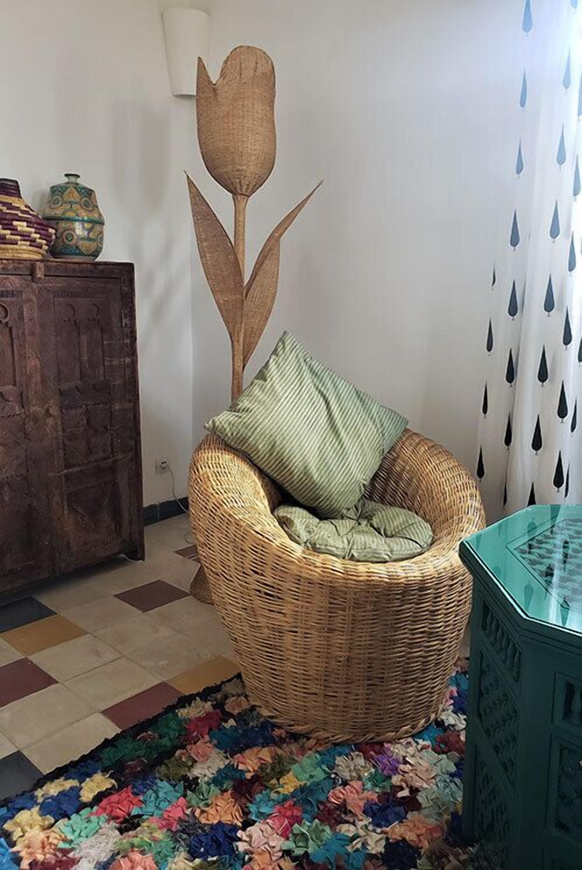 Una silla de mimbre con cojín, una alfombra colorida, un armario de madera y un adorno floral en la pared.