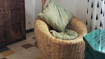 Una silla de mimbre con cojín, una alfombra colorida, un armario de madera y un adorno floral en la pared.
