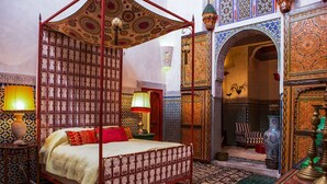 Une chambre marocaine traditionnelle avec un lit à baldaquin, des motifs complexes de carreaux de céramique et un arc décoratif.