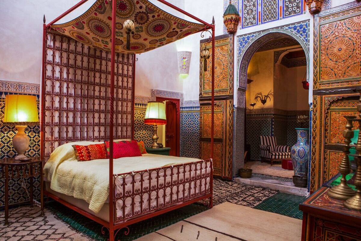 A traditional Moroccan room with a four-poster bed, intricate tile work, and a decorative archway.
