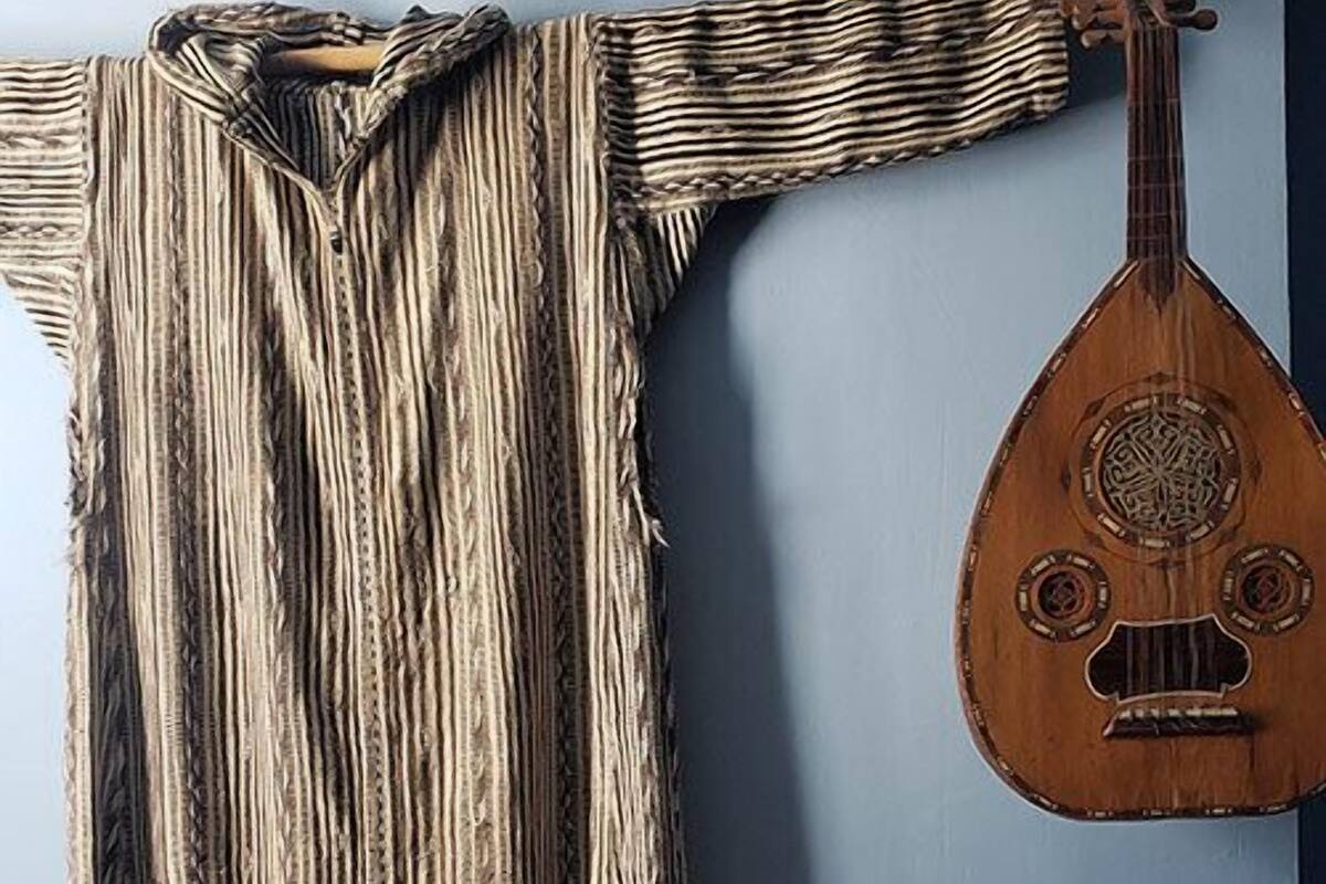 A room with a hanging garment, a wooden instrument, a lamp, and a woven vase.