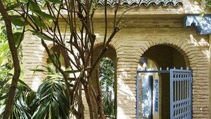 Une cour avec un bâtiment en pierre, une porte bleue et une végétation luxuriante.