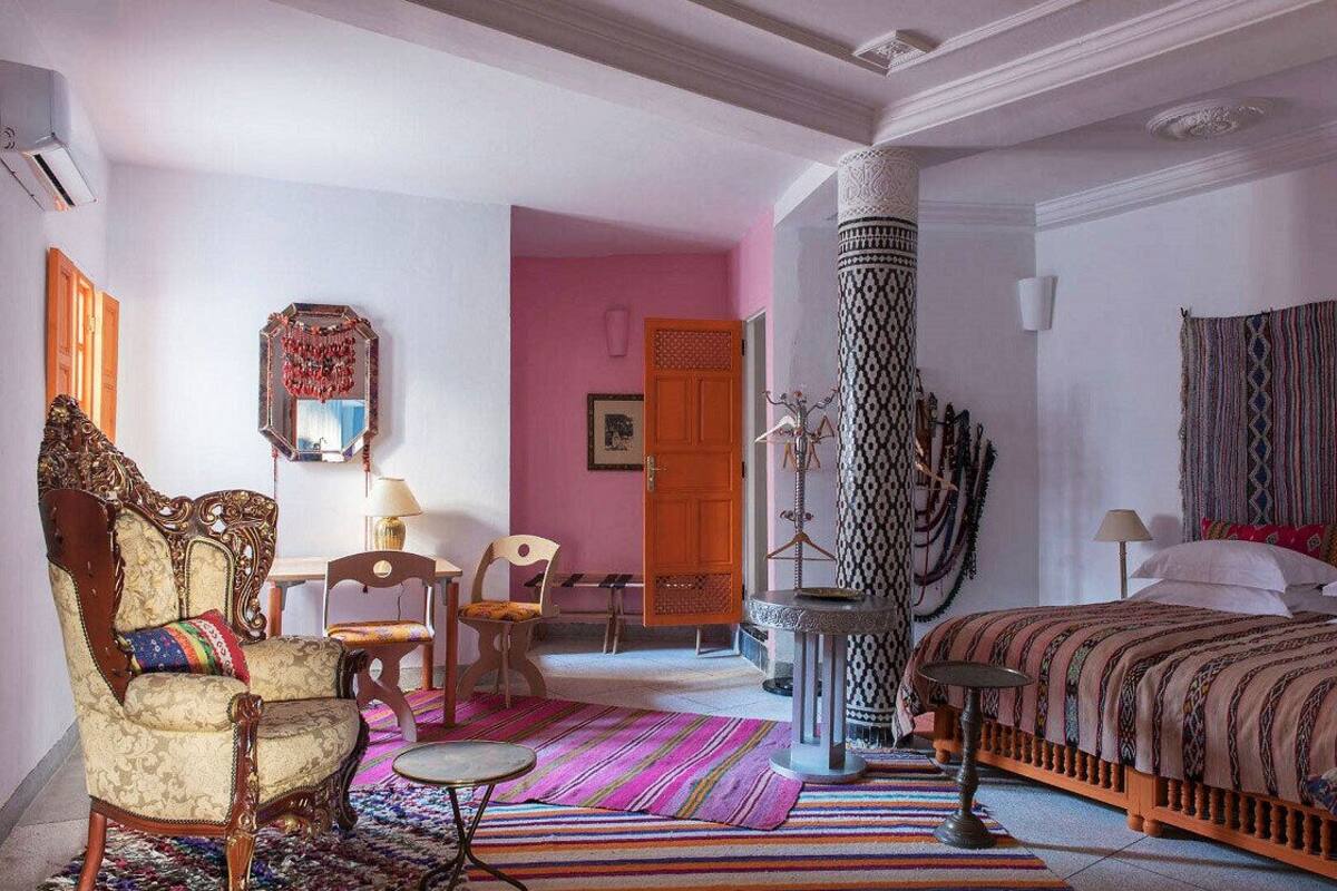 A room with a bed, a chair, a table, a mirror, and a door.