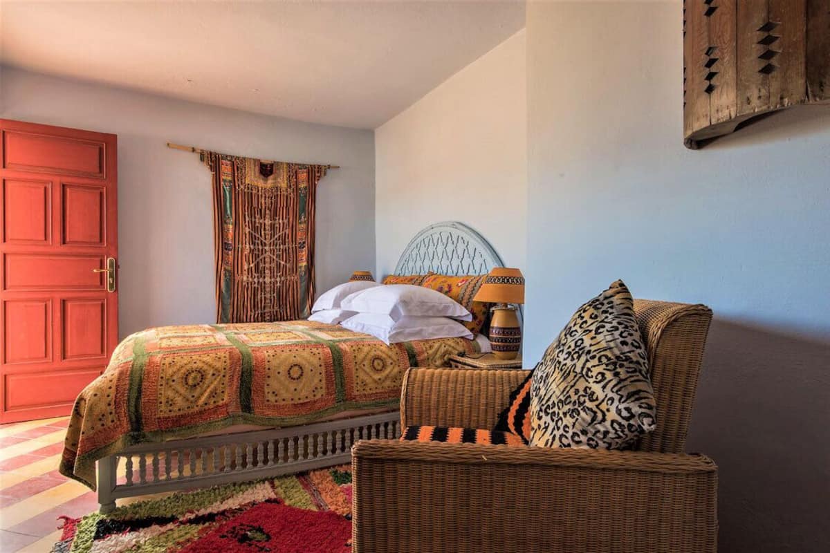 A bedroom with a bed, a wicker chair, a nightstand, and a red door.