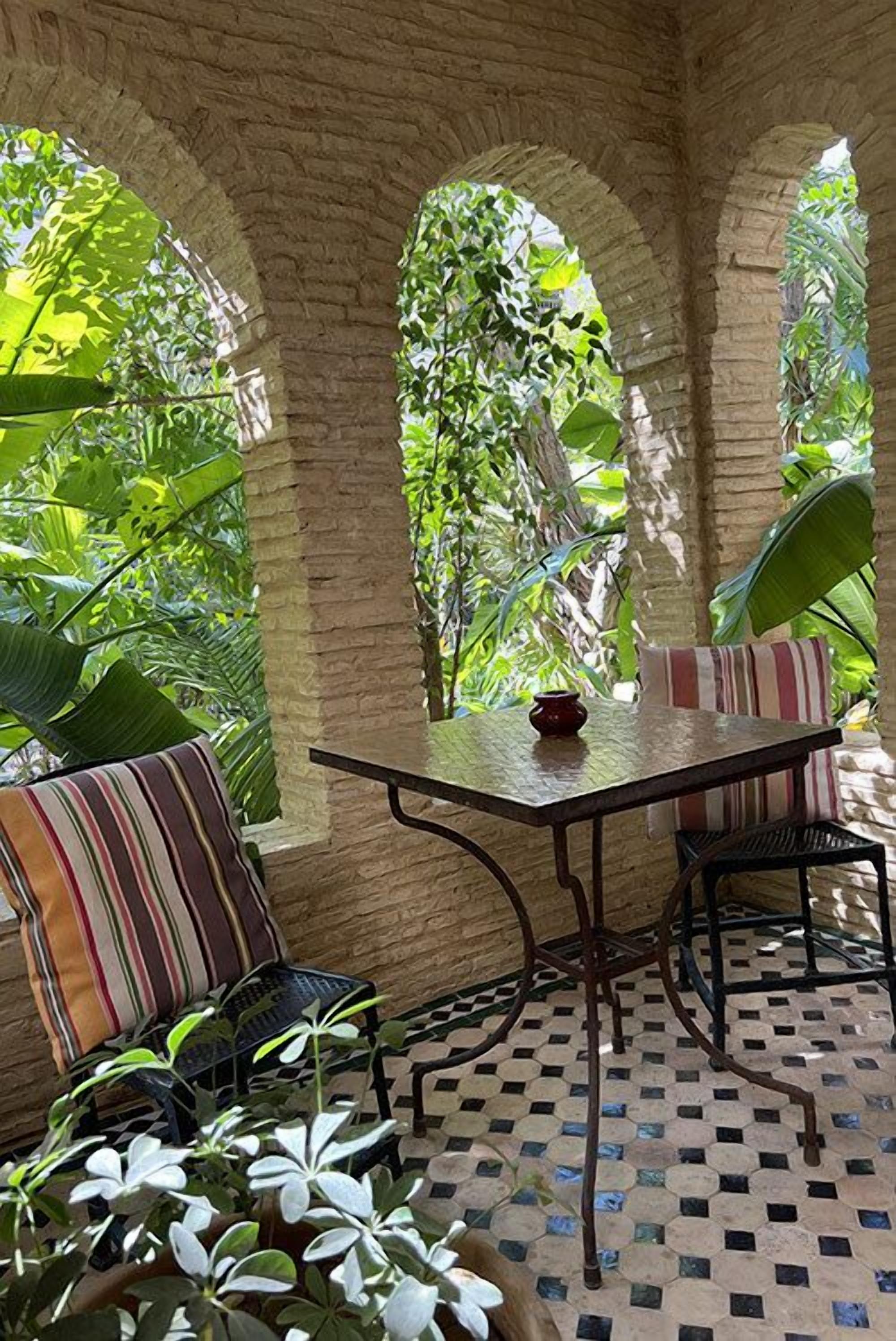Un espace patio accueillant, avec une table et des chaises, entouré d’une végétation luxuriante et d’arcs en pierre.