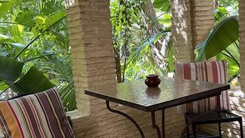 Un espace patio accueillant, avec une table et des chaises, entouré d’une végétation luxuriante et d’arcs en pierre.