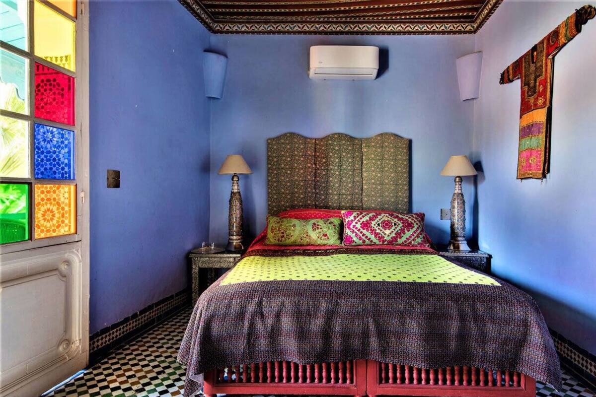 A room with a checkered floor, a bed with patterned bedding, two bedside lamps, and a decorative headboard.