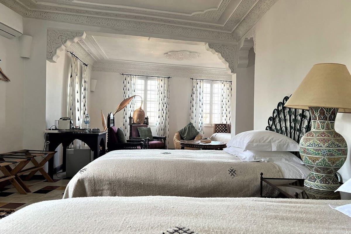 A hotel room with two beds, a desk, a chair, a lamp, and a decorative vase.