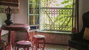 Une pièce dotée d’un sol carrelé, d’une table avec des chaises, d’un canapé et d’une fenêtre ornée de vitraux aux couleurs vives.