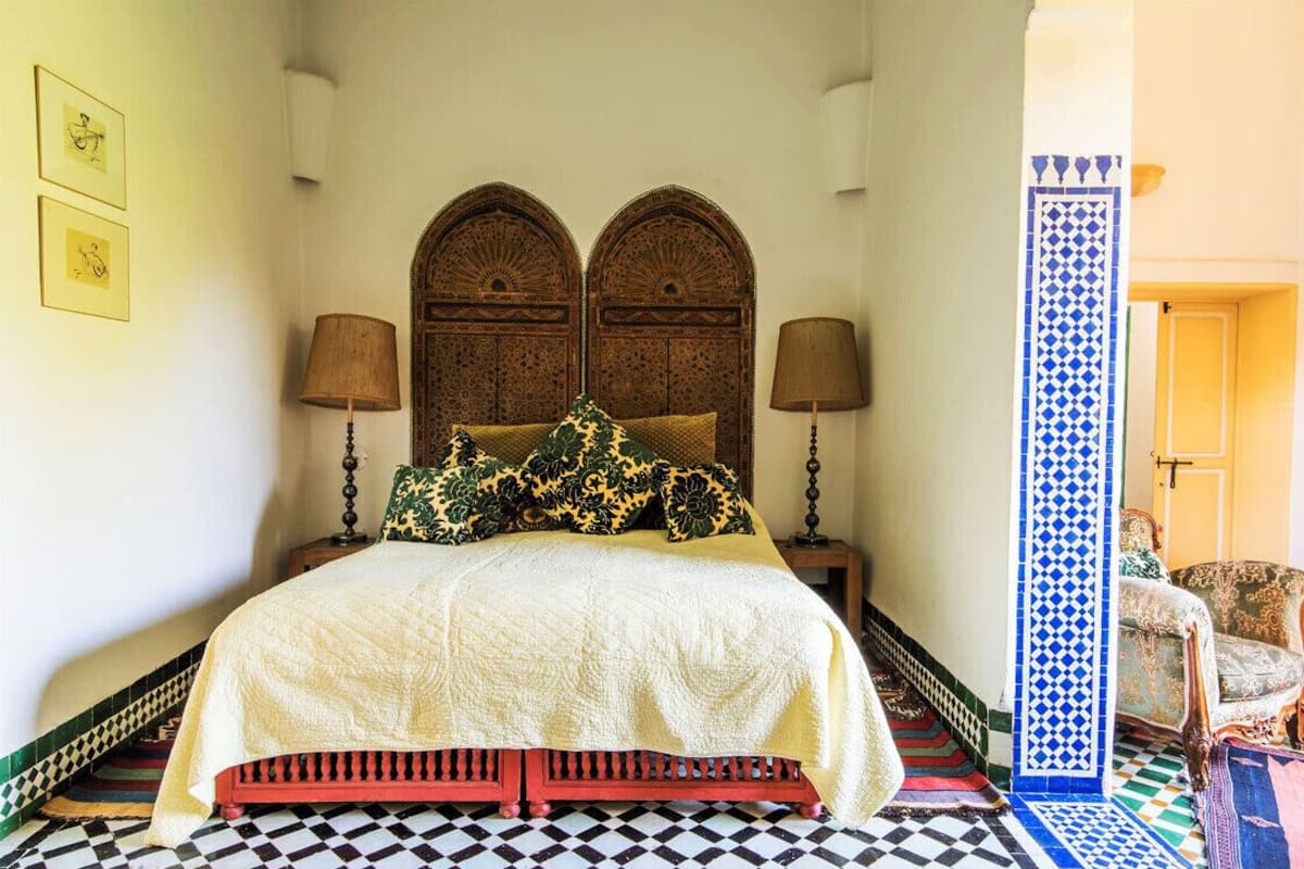 A traditional room with a bed, two lamps, a patterned floor, and a decorative wall panel.