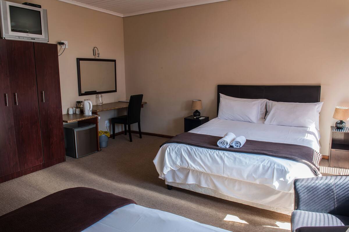 A hotel room with a bed, a desk, a chair, a television, and a wardrobe.