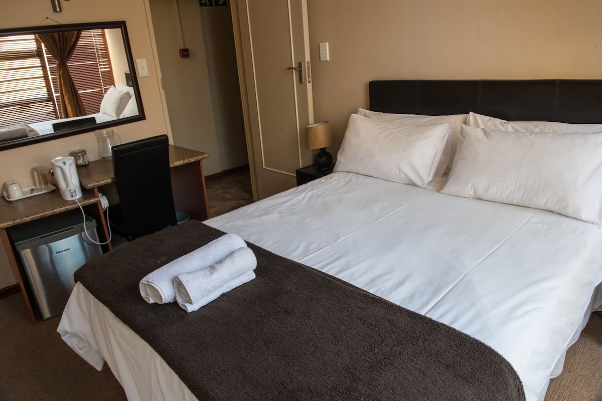 A hotel room with a bed, a desk with a telephone and a coffee maker, a mirror, and a door.