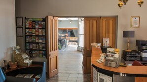 En receptionsdisk i træ, et siddeområde med en blå stol, en reol med brochurer og udsigt til et køkken.