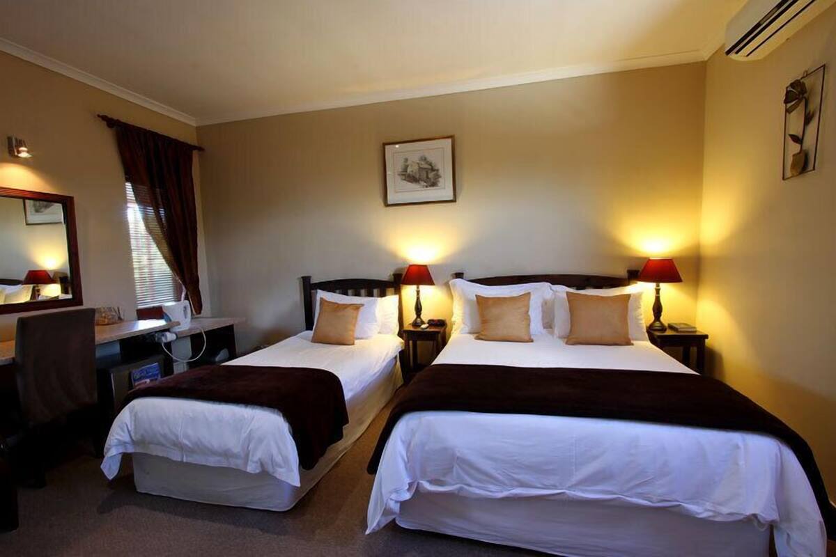 A hotel room with two single beds, a desk with a chair, a mirror, and two bedside lamps.