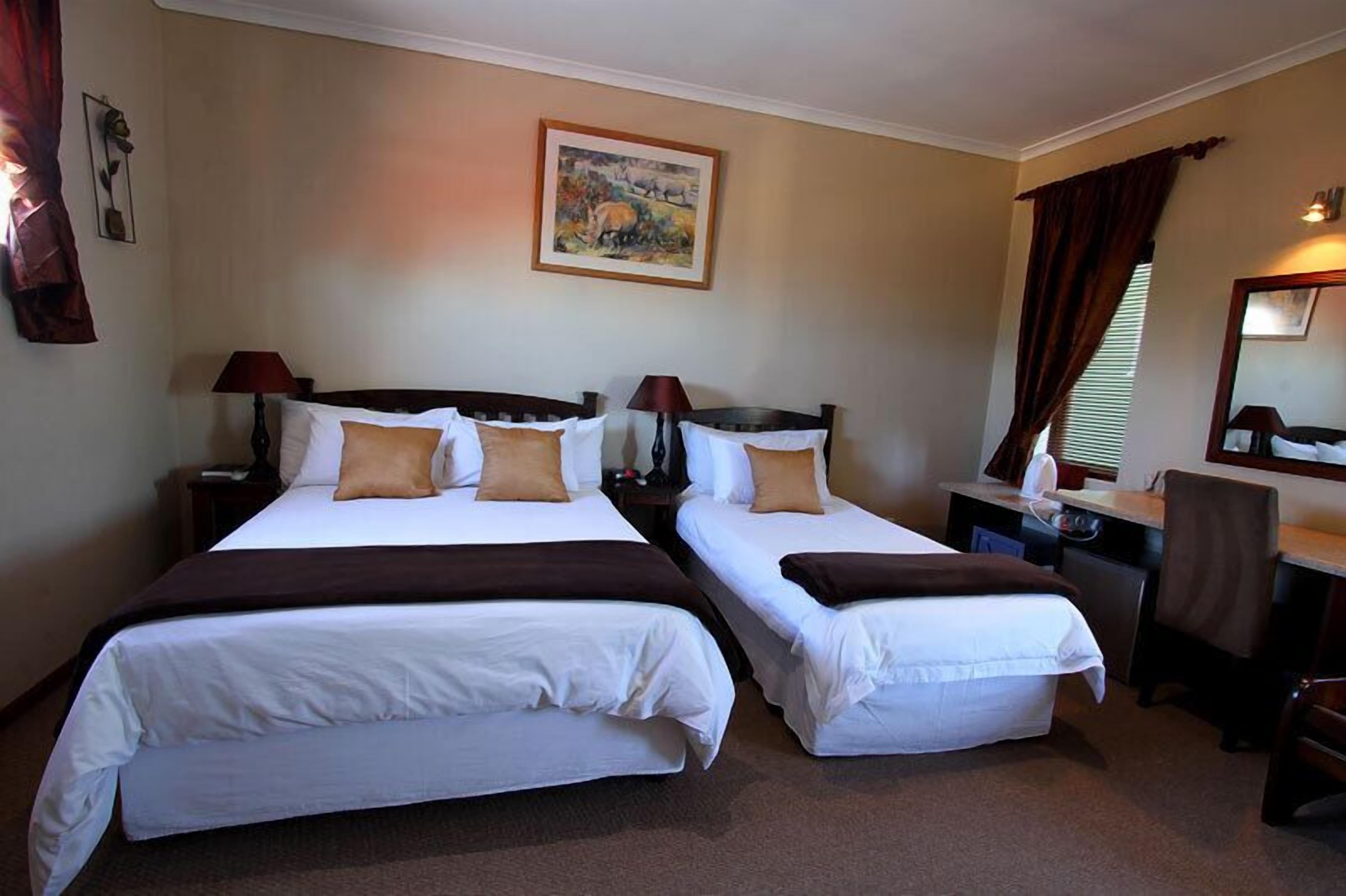 A hotel room with two single beds, a desk, a chair, a lamp, and a painting on the wall.