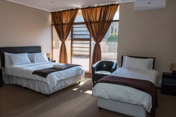 A hotel room with two beds, a chair, and a window with curtains. - Ramasibi Guest Services (Cape Town)