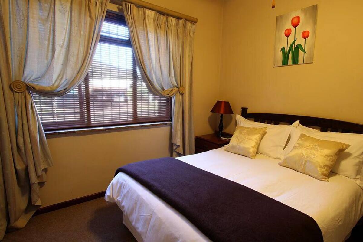 A hotel room with a bed, curtains, a painting, and a nightstand.