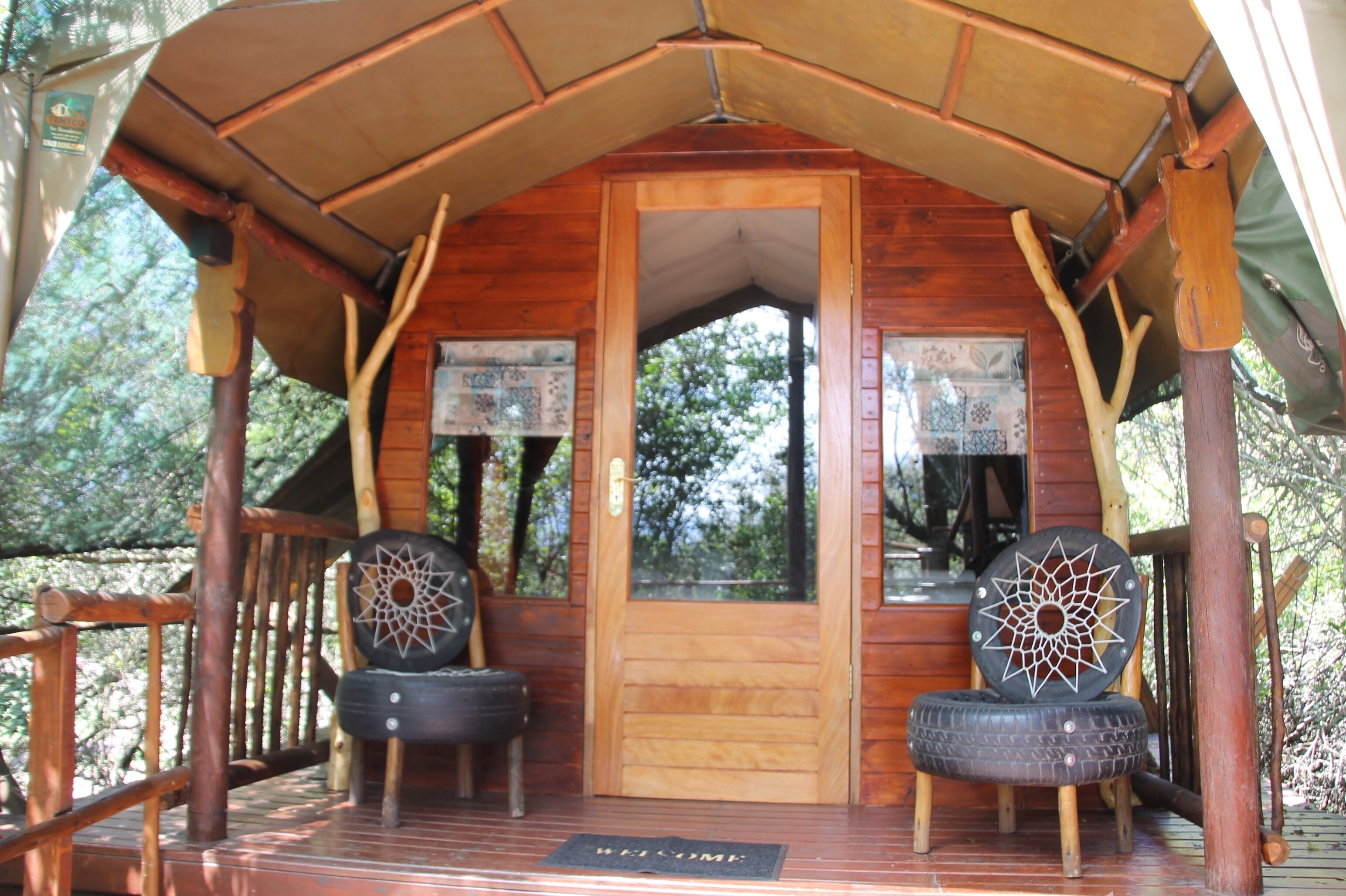 A wooden cabin with a porch, a door, and two tire chairs with decorative patterns.