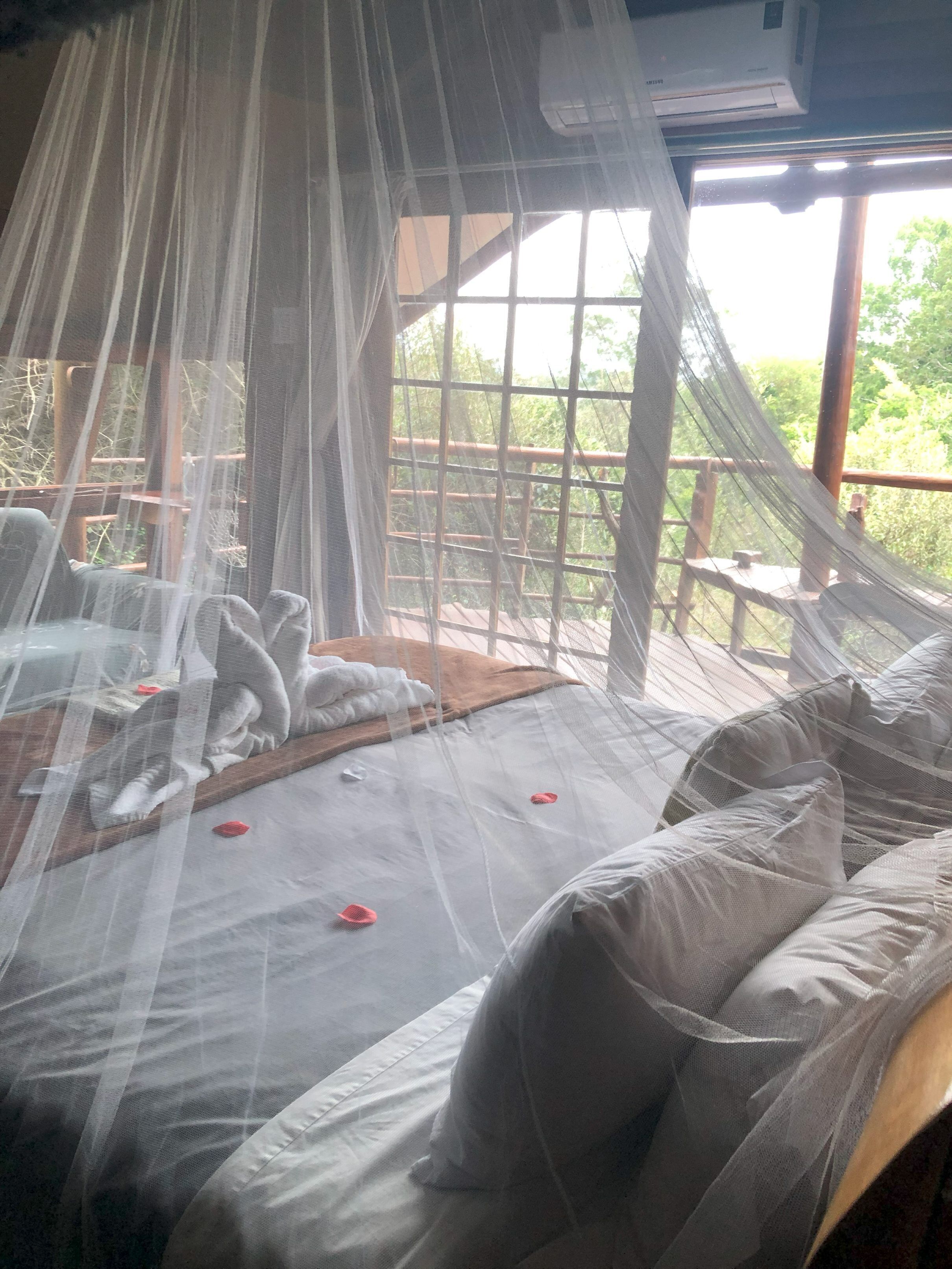 Ein Zimmer mit einem Moskitonetz über dem Bett, einem Holz-Kopfteil und Blick auf Grünfläche.