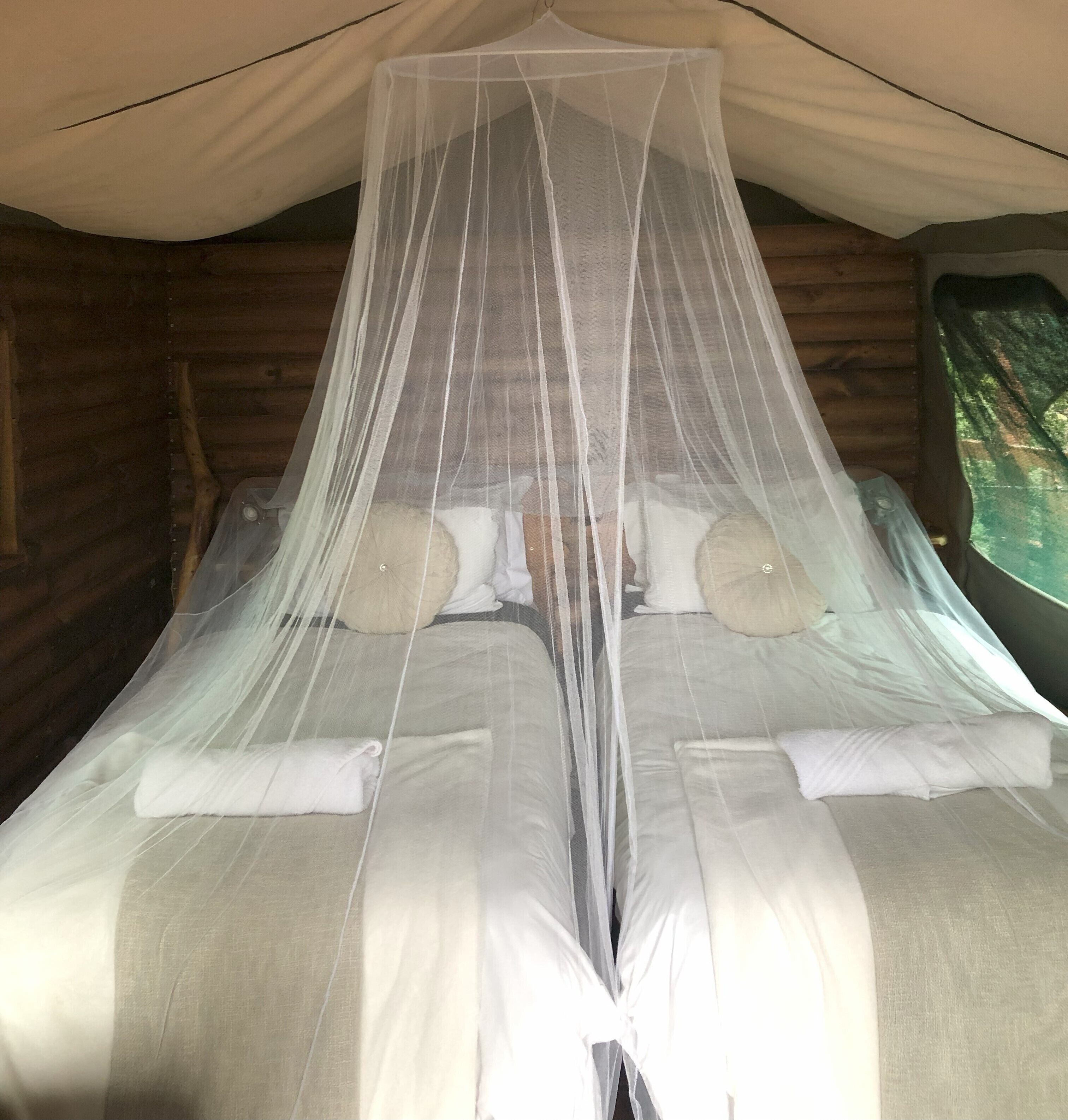 A bed with a mosquito net, pillows, and a blanket in a tent-like room with wooden walls.