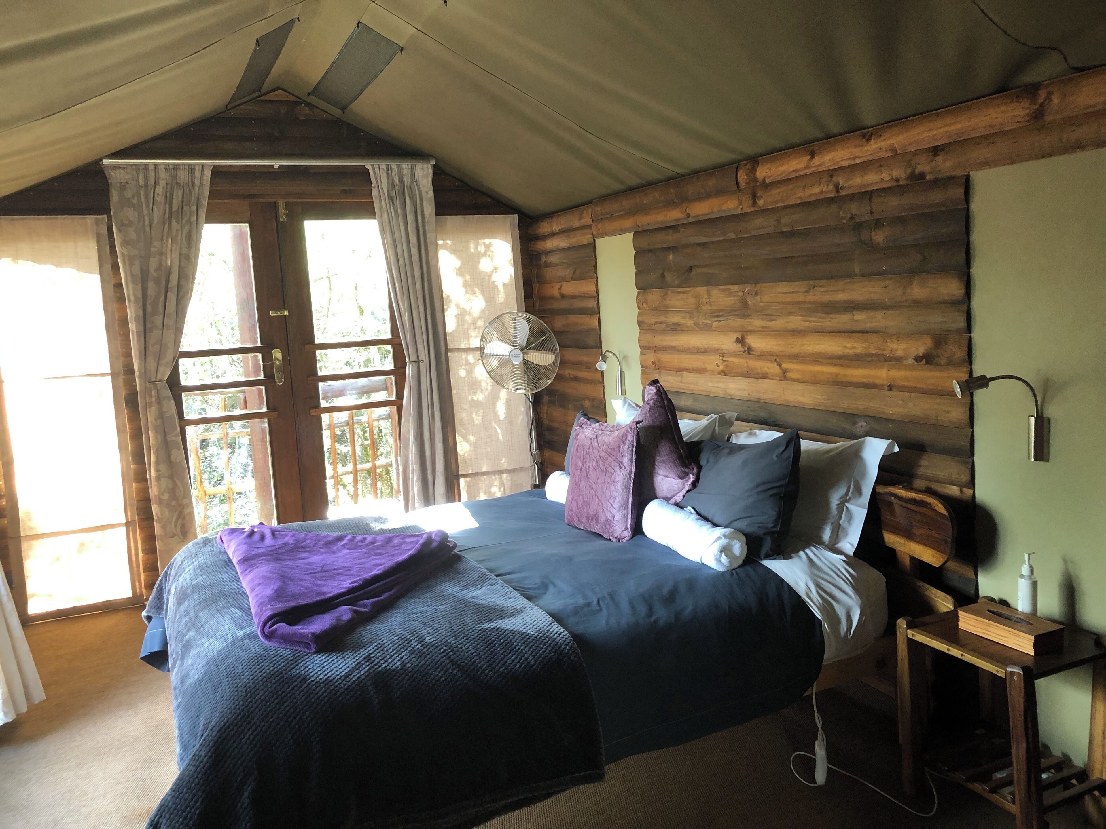 A cozy room with a bed, a fan, and a nightstand.