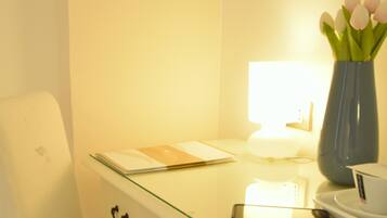 A hotel room with a glass desk, a smartphone, a vase with flowers, a cup, and a book.