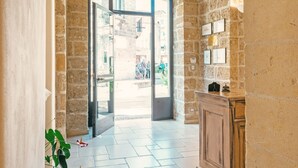 An interior with a stone archway leading to a door, a wooden counter, and a tiled floor. - Hotel L'Arcangelo Boutique Hotel (Taranto)