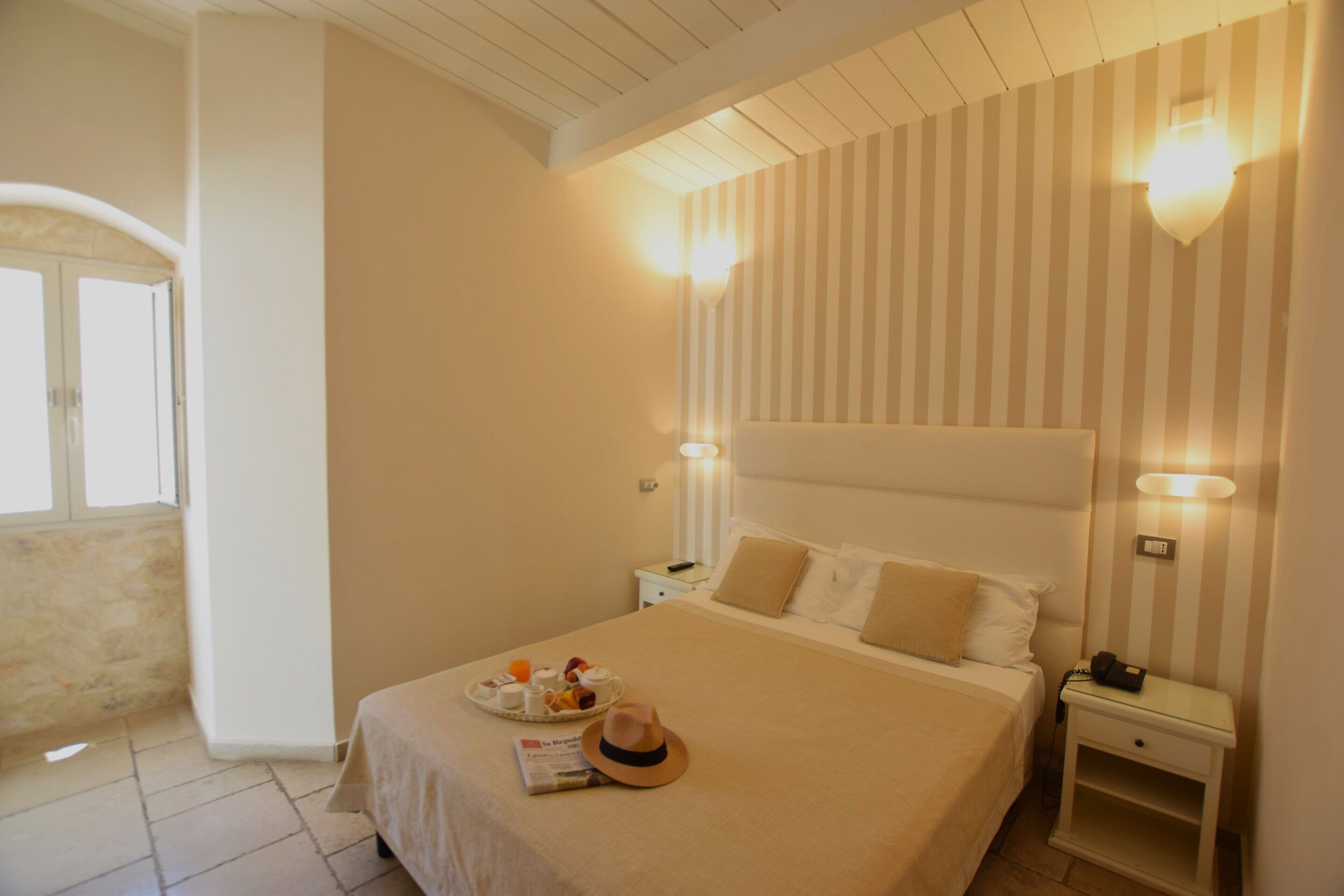 Ein Hotelzimmer mit einem großen Bett, einem Nachttisch mit Lampe und einem Fenster mit Vorhängen.