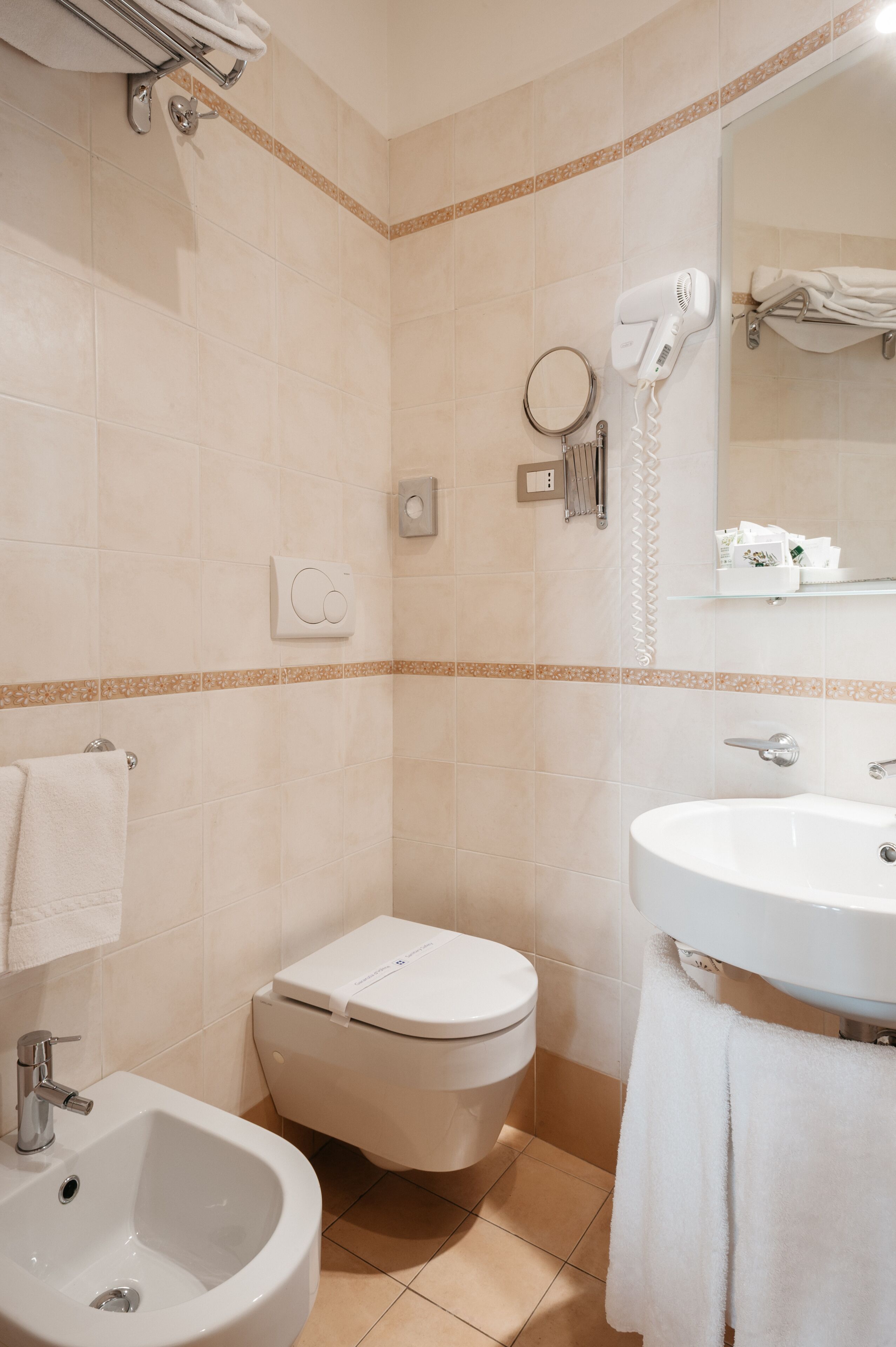 Un baño con inodoro, bidé, lavamanos y un secador de pelo en la pared.