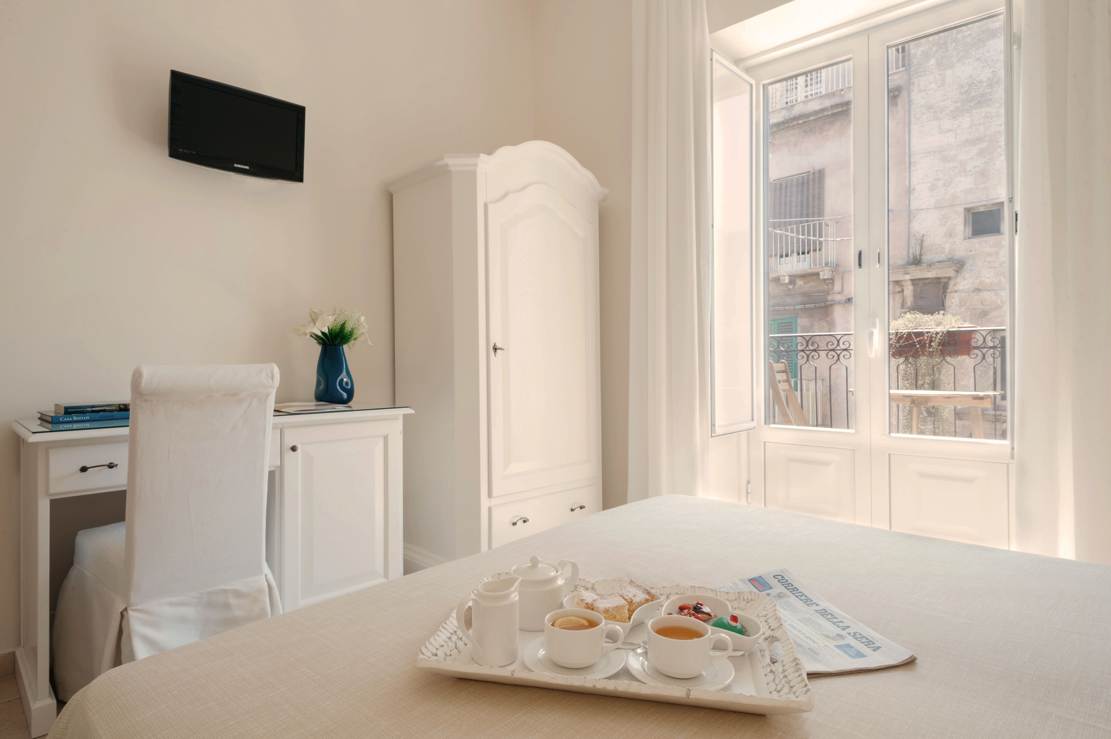 Une chambre d’hôtel comprenant un lit, un bureau avec une chaise, un téléviseur fixé au mur, une armoire et une fenêtre donnant sur des immeubles.