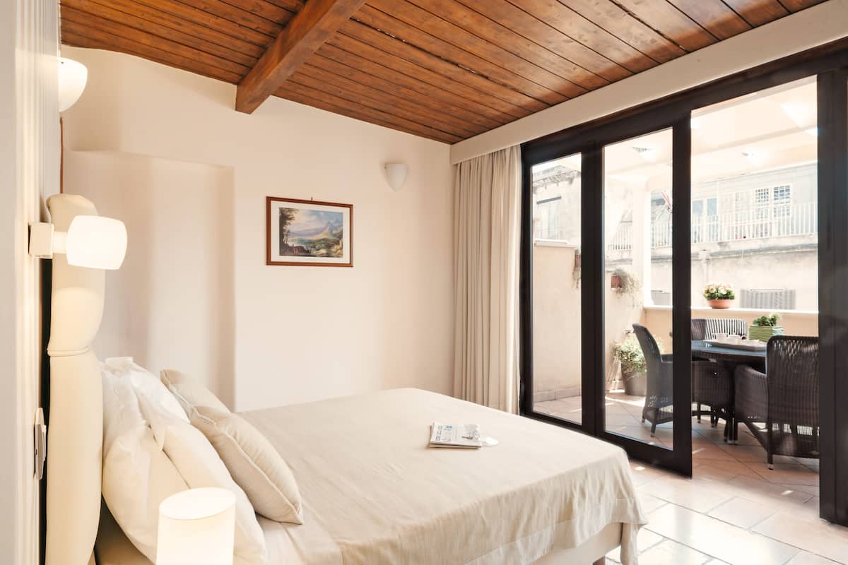 A bedroom with a bed, a window, and a view of an outdoor balcony.