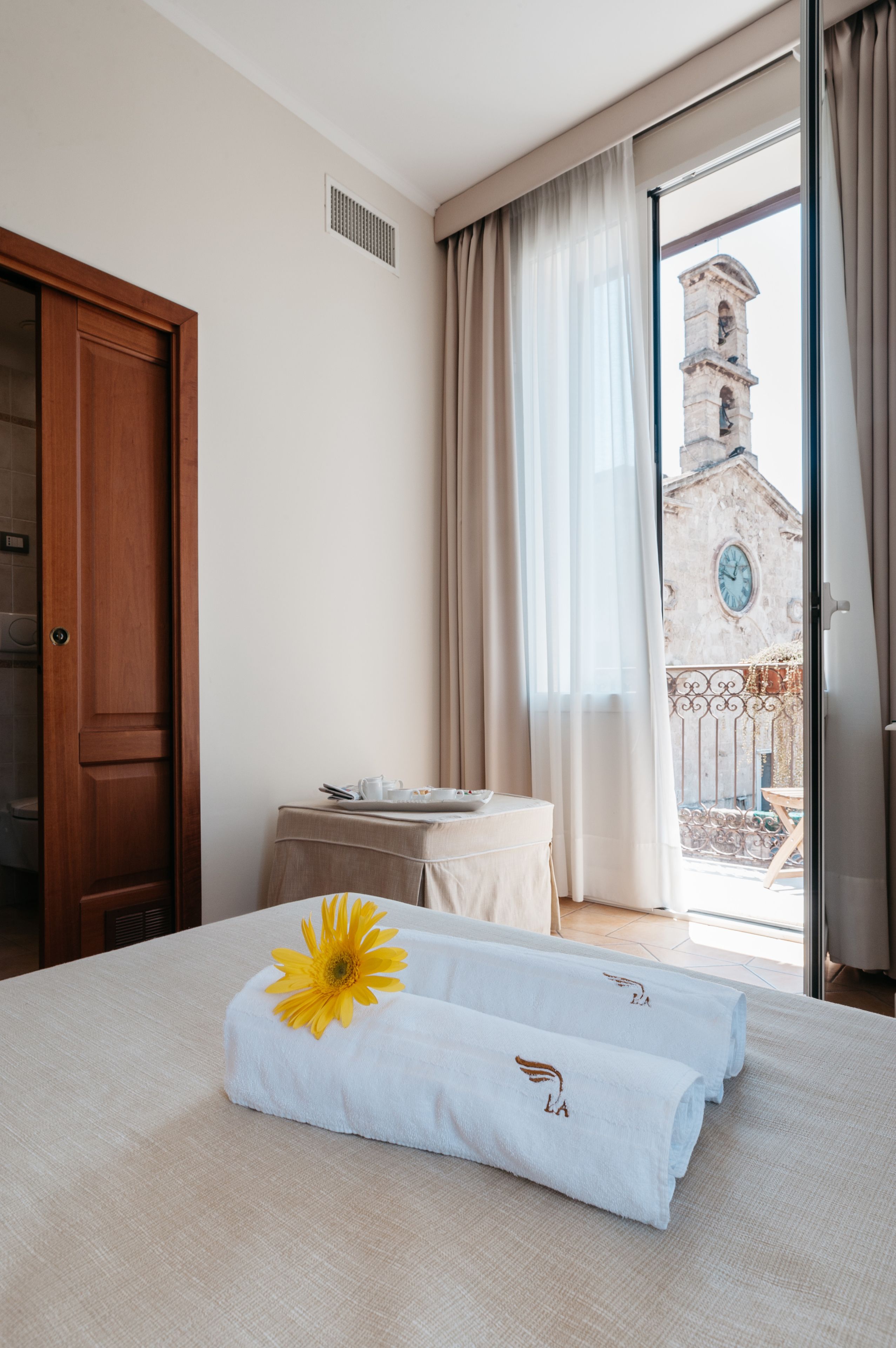 A hotel room with a bed, a table with a tray, a window with curtains, and a view of a building outside.