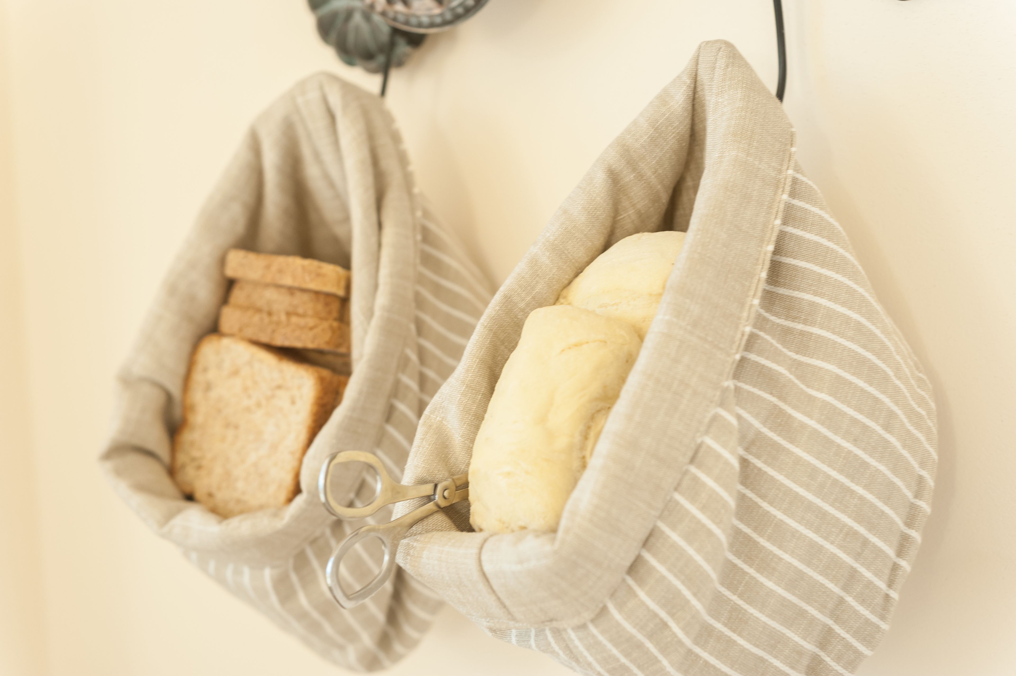 Two fabric bags hanging on a wall, one containing bread and the other containing a loaf of bread.