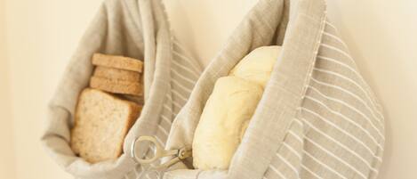 Two fabric bags hanging on a wall, one containing bread and the other containing a loaf of bread.