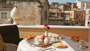 A table set with breakfast items, a wicker chair, and a vase with flowers, overlooking a cityscape. - Hotel L'Arcangelo Boutique Hotel (Taranto)