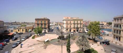 A square with a fountain, surrounded by buildings and parked cars.