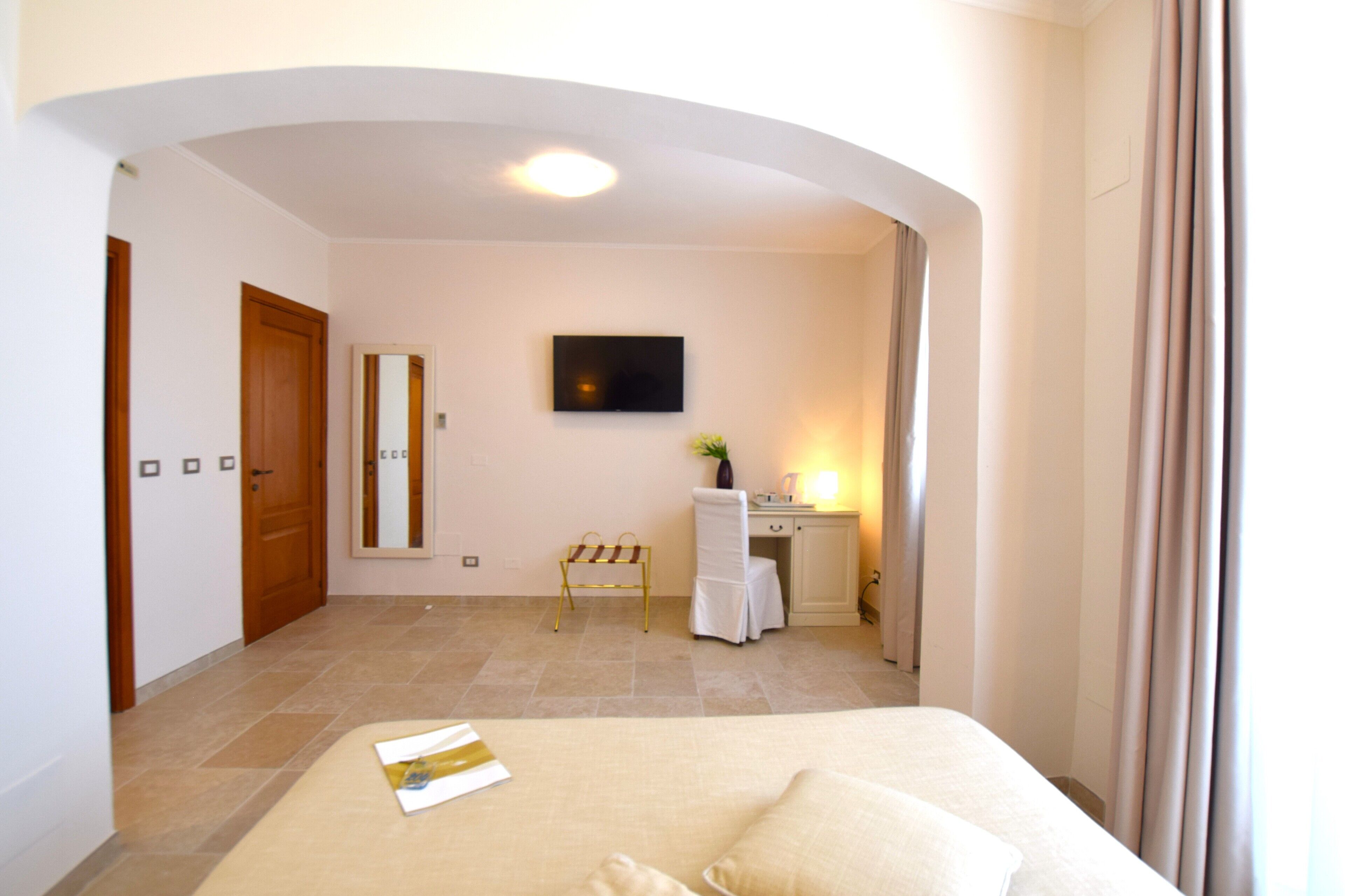 Une chambre d’hôtel avec un lit, un bureau, une chaise, une télévision et une petite table sur laquelle se trouve un vase.