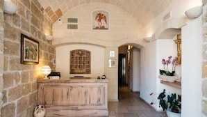 A reception area with a stone wall, wooden reception desk, and a ceiling mural. - Hotel L'Arcangelo Boutique Hotel (Taranto)