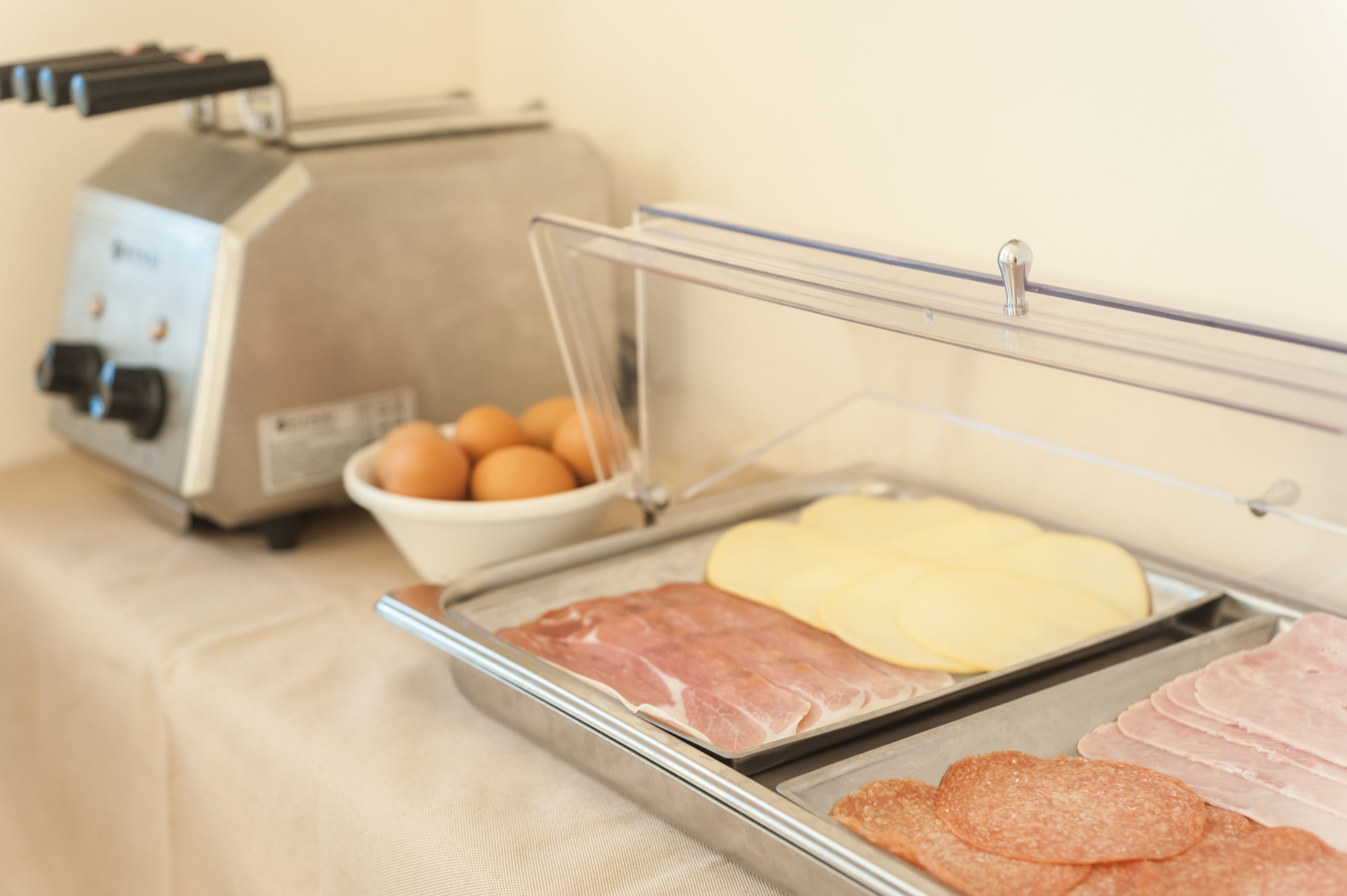 A breakfast buffet with various food items including eggs, cheese, ham, and sausages.