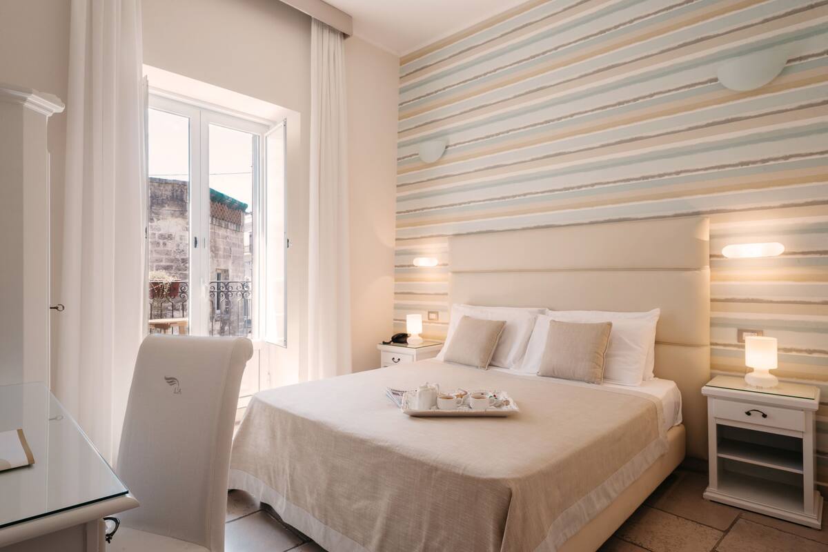 A hotel room with a bed, bedside tables, a chair, and a view of the outside.