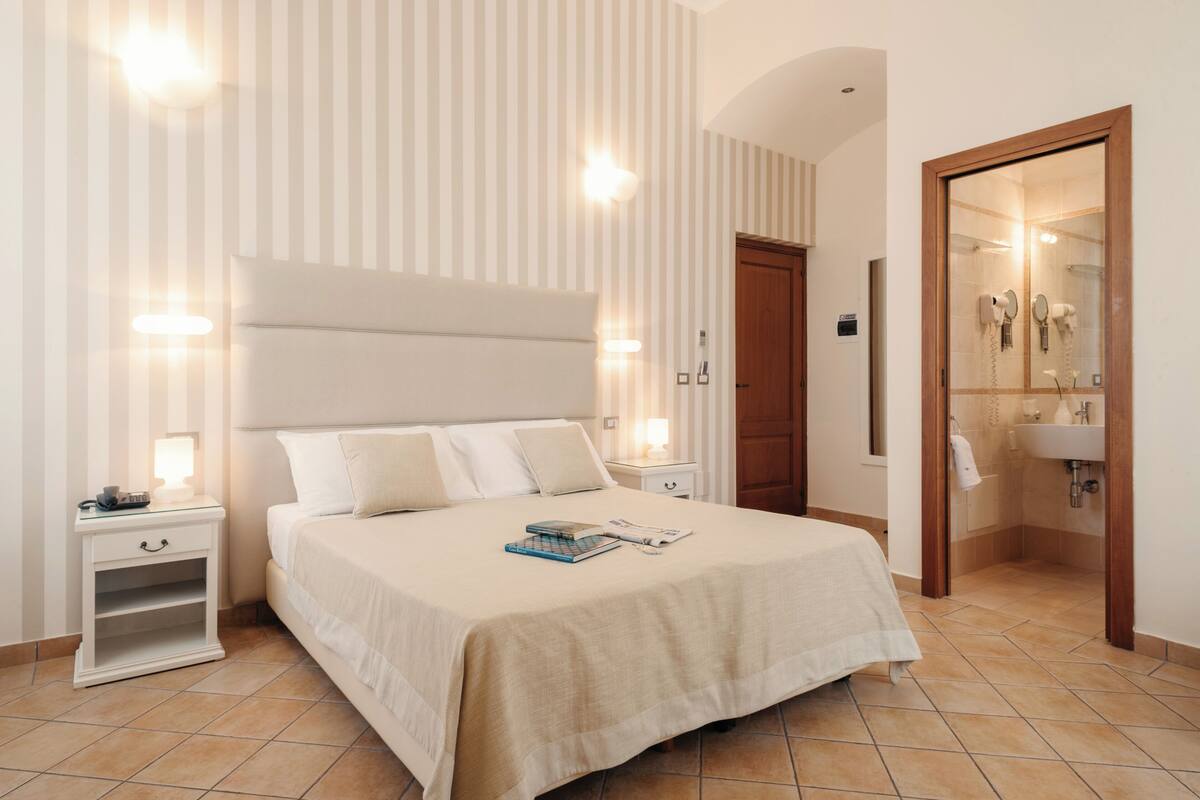 A neatly arranged bedroom with a large bed, bedside tables, and a bathroom visible through an open door.