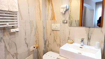 Un bagno moderno con parete in marmo, lavandino bianco, bidet e asciugacapelli montato a parete.