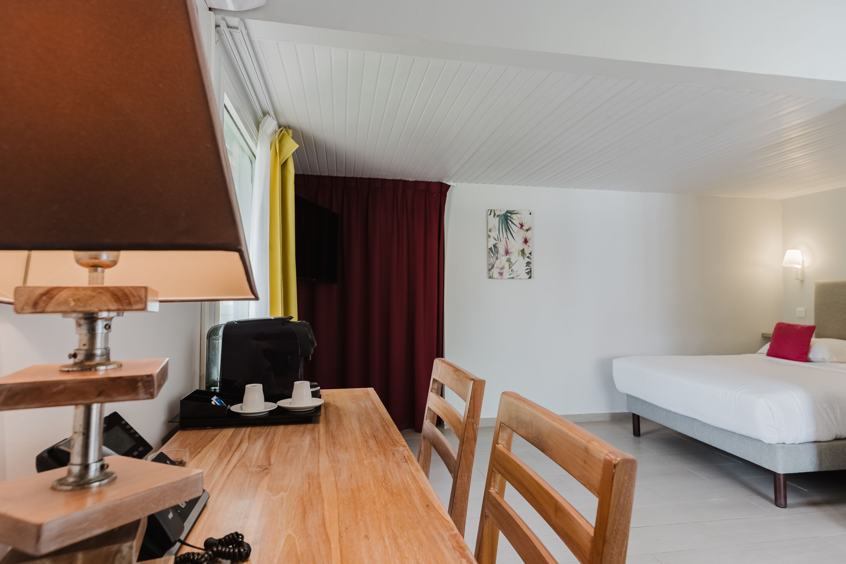 A room with a wooden table, chairs, a bed, and a desk with a lamp.