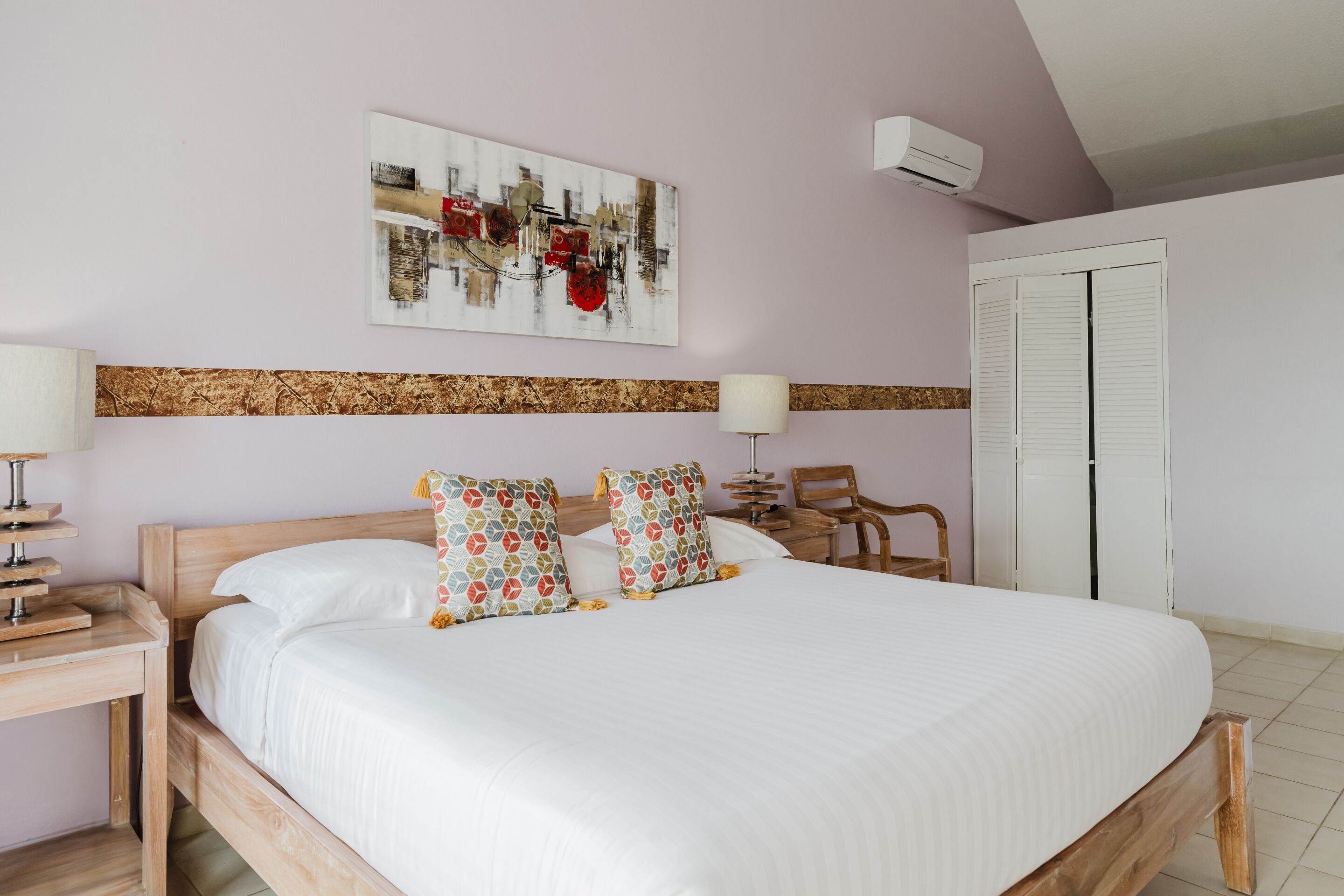 A bedroom with a bed, a nightstand, a chair, a wall-mounted air conditioner, and a door.
