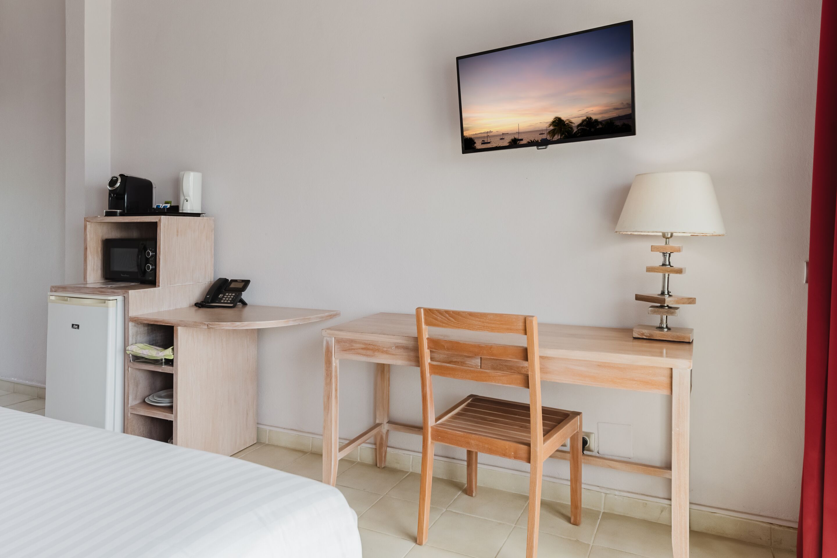 A hotel room with a bed, a desk with a chair, a small refrigerator, a microwave, a telephone, a television mounted on the wall, and a table lamp.