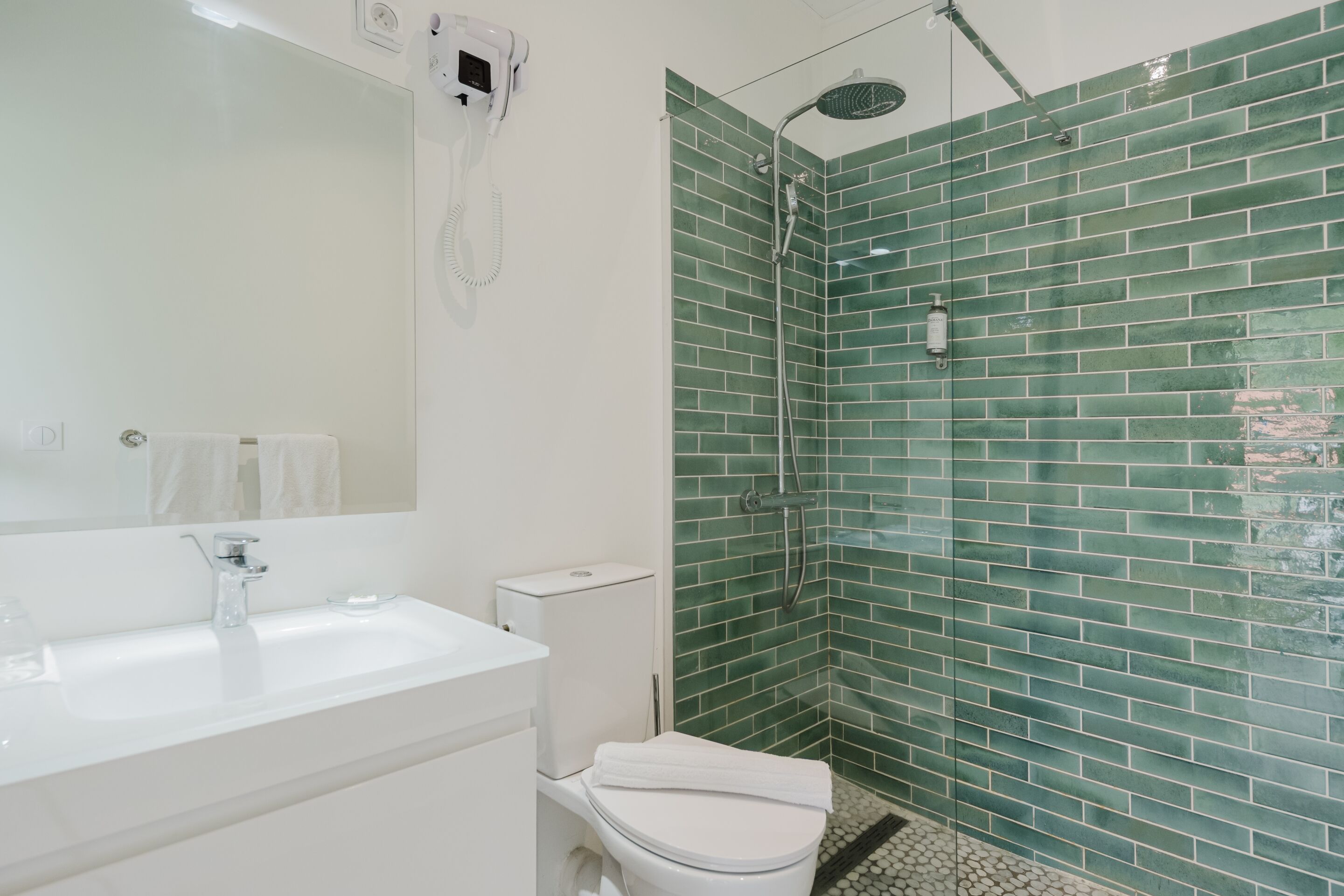A bathroom with a white sink, toilet, and a glass-enclosed shower area with green tiles.
