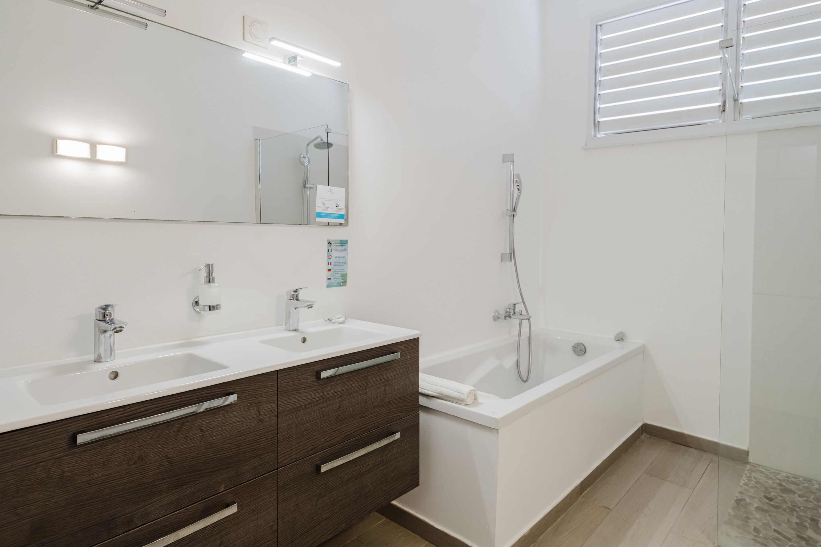 Un baño moderno con tocador de doble lavabo, un espejo grande, bañera y ducha.